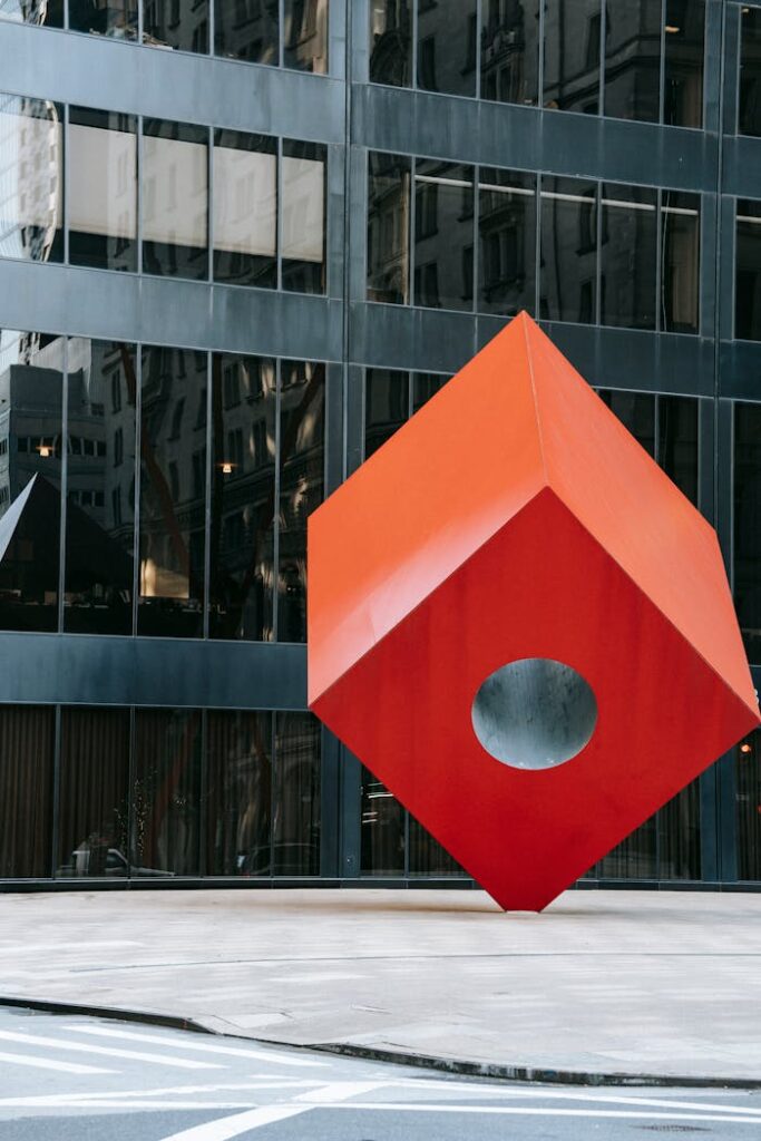 Creative geometric construction of red cube on street in downtown of modern city